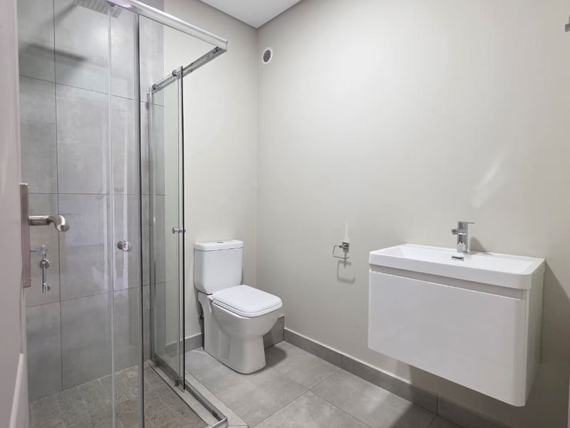 Modern bathroom featuring a glass-enclosed shower, wall-mounted vanity, and neutral tiled finishes in excellent condition.
