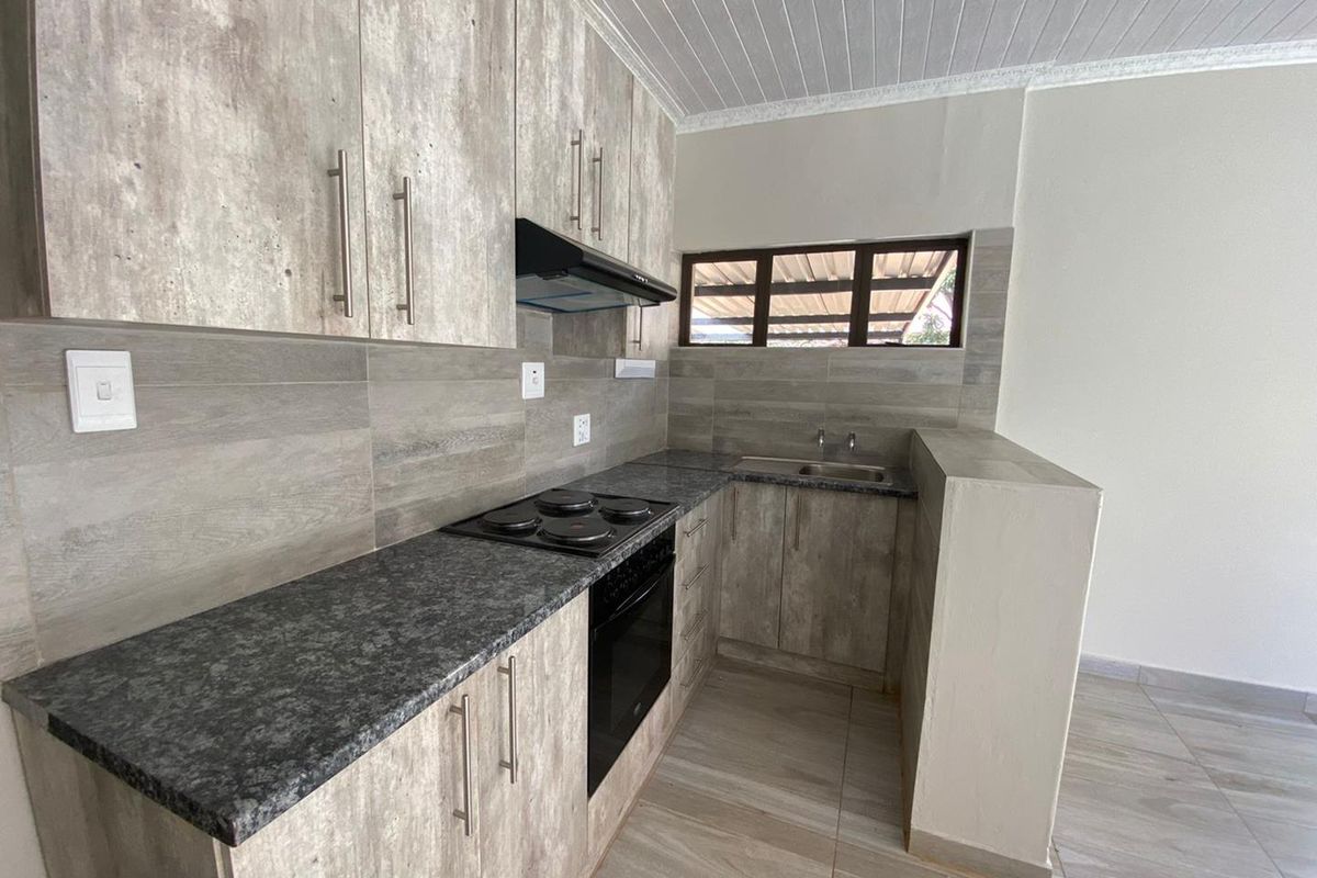 Modern kitchen featuring wood-look cabinetry, granite countertops, a built-in electric hob and oven, extractor fan, and tiled backsplash.