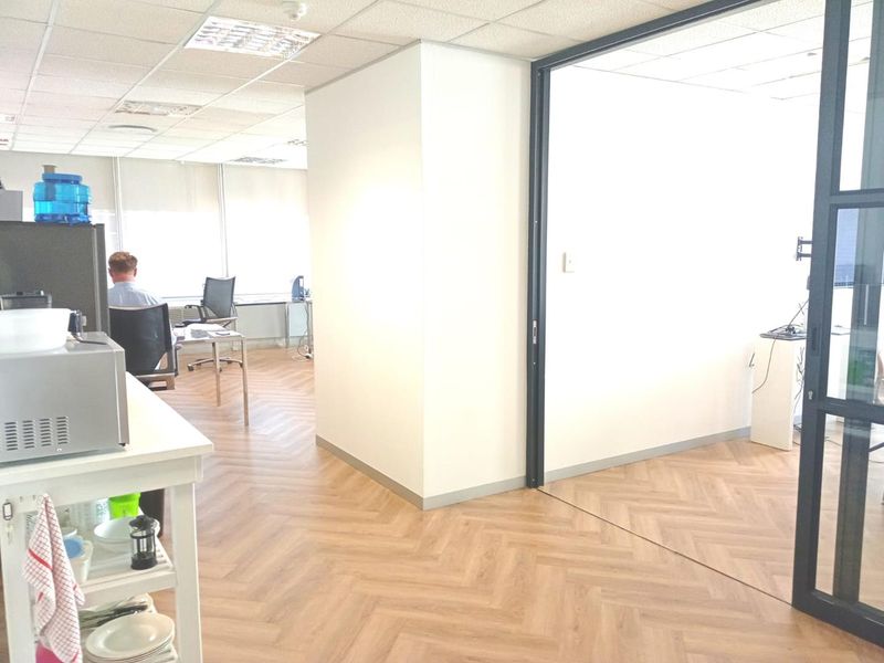 Modern office space featuring herringbone flooring, suspended ceiling tiles, and a sleek black-framed glass partition separating work areas.