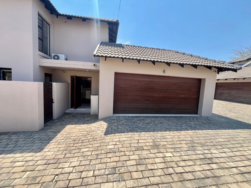 Front exterior view of a townhouse featuring a paved driveway, double garage with wooden door, and tiled roof.