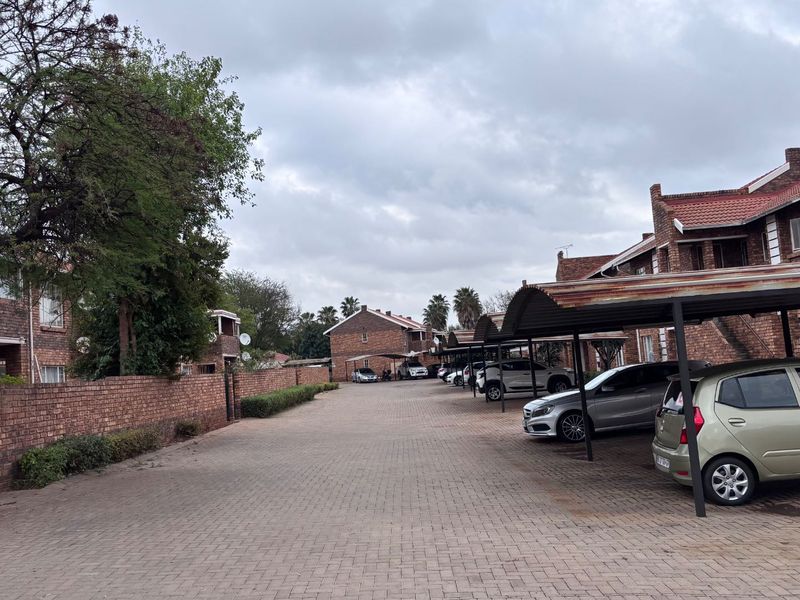 Exterior view of an apartment complex featuring a paved driveway, brick building facades, and covered parking bays.