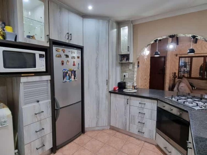 A functional kitchen featuring light wood-grain cabinetry, granite countertops, a gas hob, and a built-in oven, connected to the living area via an archway.