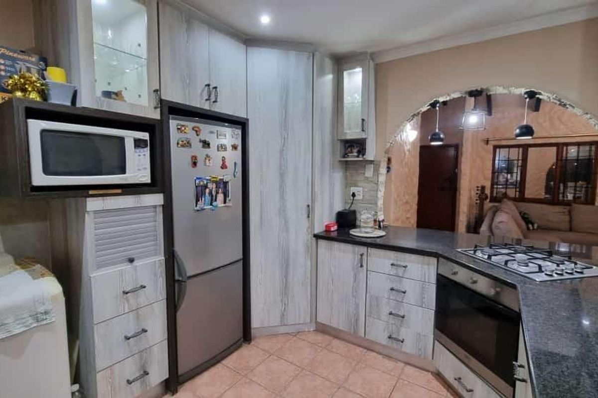 A functional kitchen featuring light wood-grain cabinetry, granite countertops, a gas hob, and a built-in oven, connected to the living area via an archway.