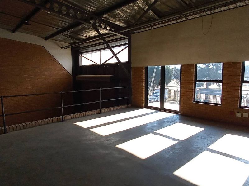 Spacious industrial mezzanine area featuring exposed brick walls, concrete flooring, and large windows providing ample natural light.