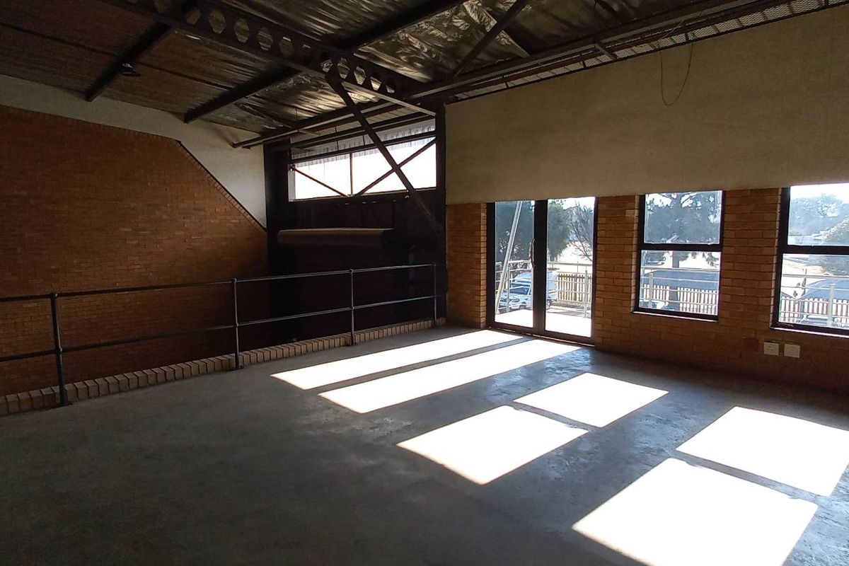 Spacious industrial mezzanine area featuring exposed brick walls, concrete flooring, and large windows providing ample natural light.