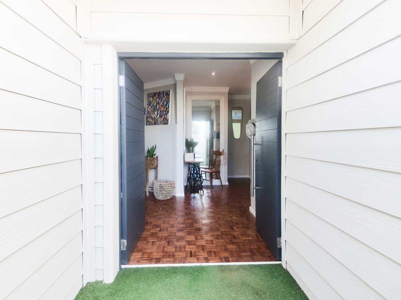 A welcoming entrance featuring double doors opening onto classic timber parquet flooring, framed by clean white weatherboard exterior cladding.
