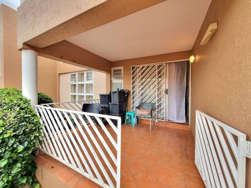 A covered patio area featuring tiled flooring, a security gate, and direct access to the interior through a sliding door.