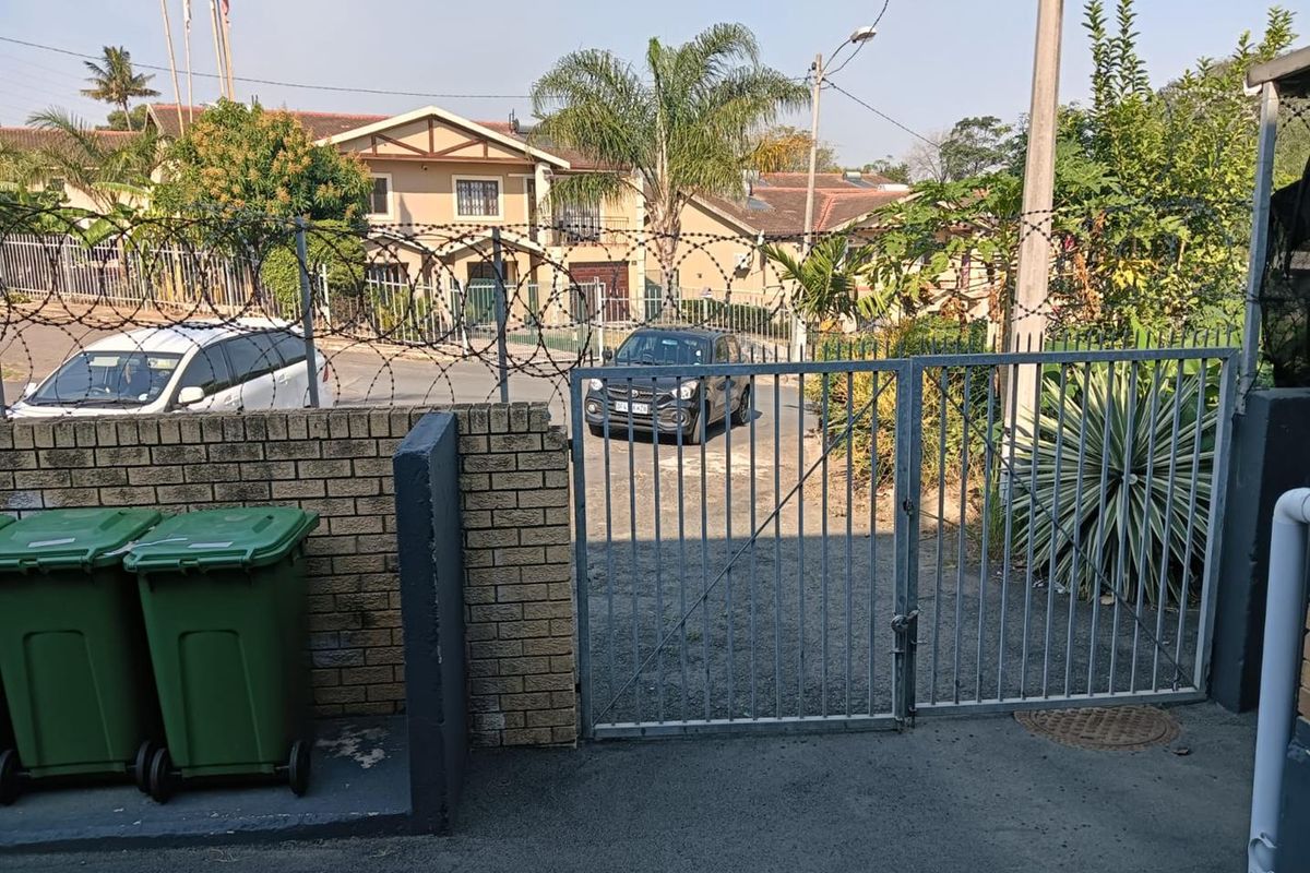 View of the property entrance featuring a metal security gate, perimeter brick wall, and razor wire fencing.