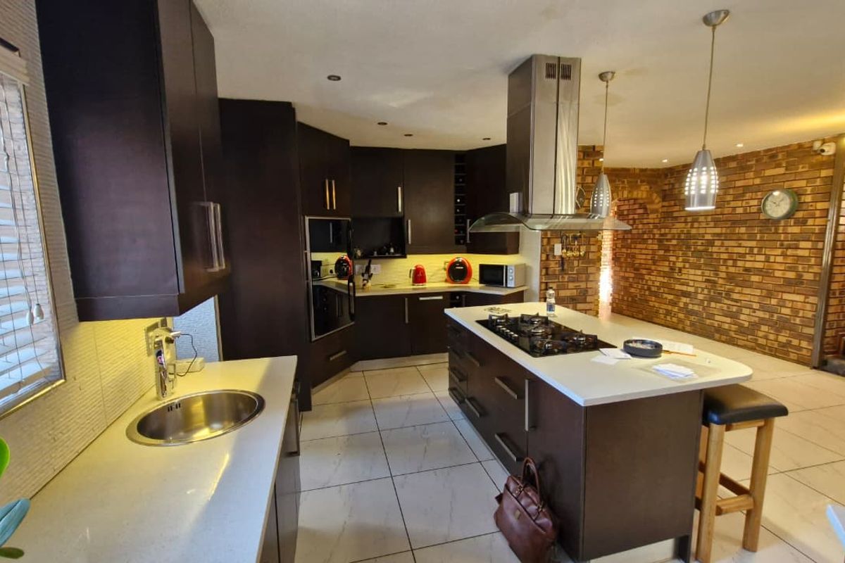 Modern kitchen featuring dark cabinetry, a central island with a gas hob, stone countertops, and an adjacent exposed brick feature wall.