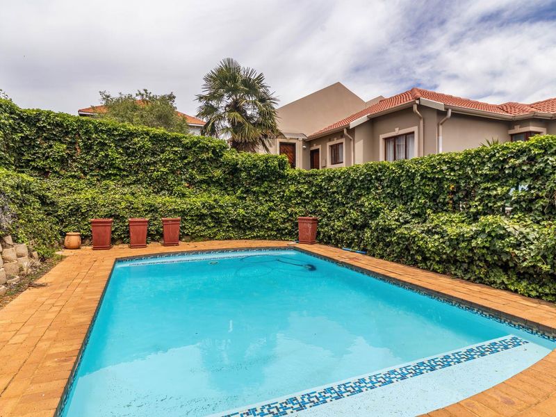 A private swimming pool area featuring paved surround, established ivy-covered boundary walls, and a view of the rear building elevation.