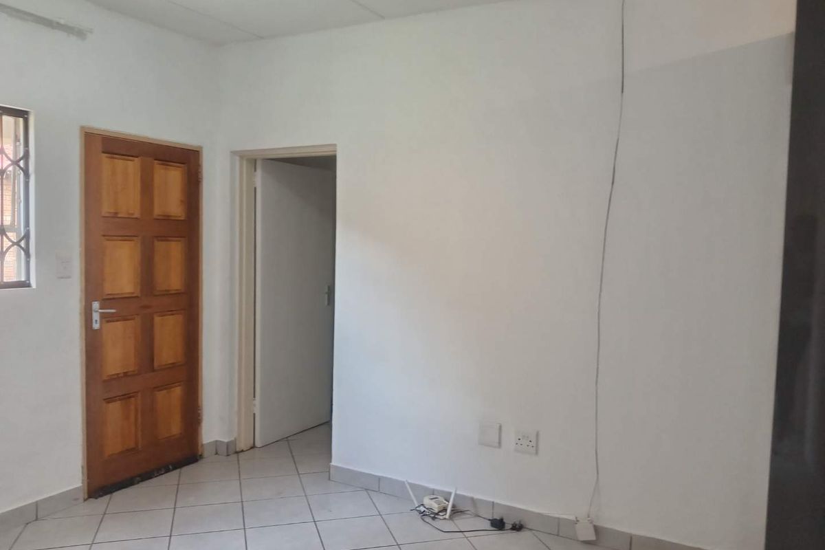 A simple, neutral interior space featuring tiled flooring, a wooden door, and access to an adjacent room.