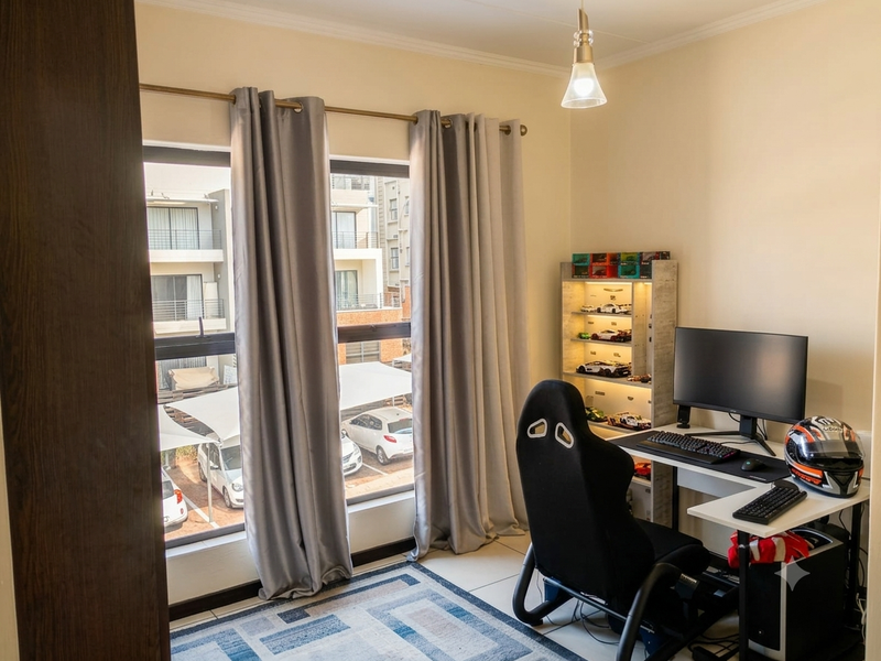 A well-lit bedroom featuring tiled flooring and large aluminium-framed windows, currently utilized as a home office space.