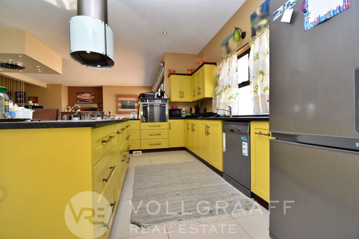 Spacious kitchen featuring bright yellow cabinetry, dark countertops, a central island, and integrated stainless steel appliances, flowing into an open-plan living area.