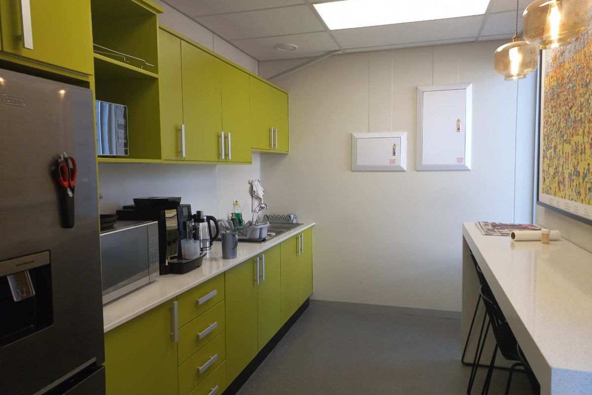 A compact office kitchenette featuring lime green cabinetry, white countertops, a stainless steel sink, and a built-in breakfast bar area.