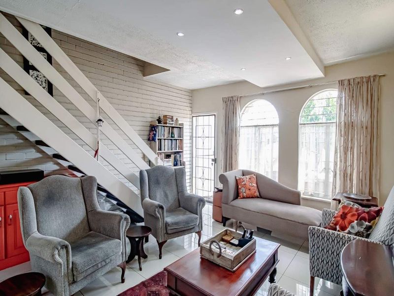 A living room featuring a staircase, arched windows, recessed ceiling lights, and tiled flooring, with a painted brick feature wall.