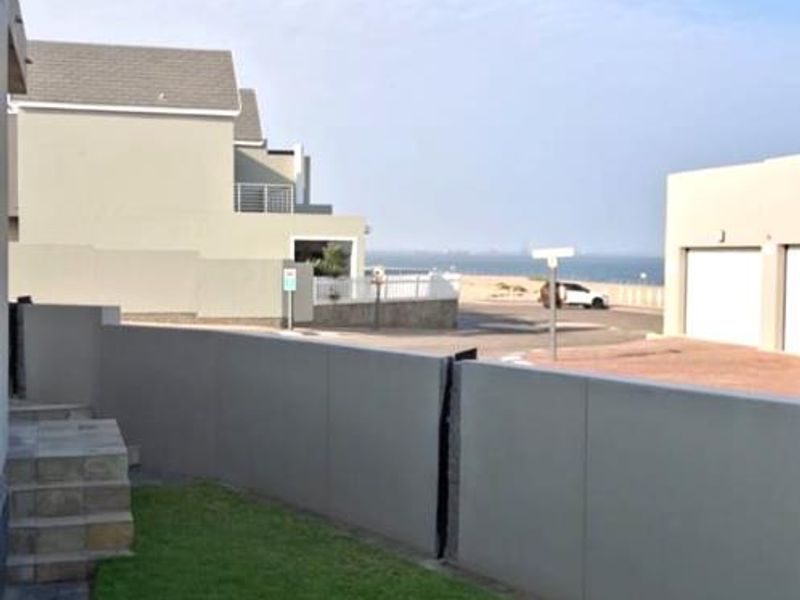 A rear exterior view of the townhouse featuring a private lawn, paved patio area, and stone steps leading to the property.