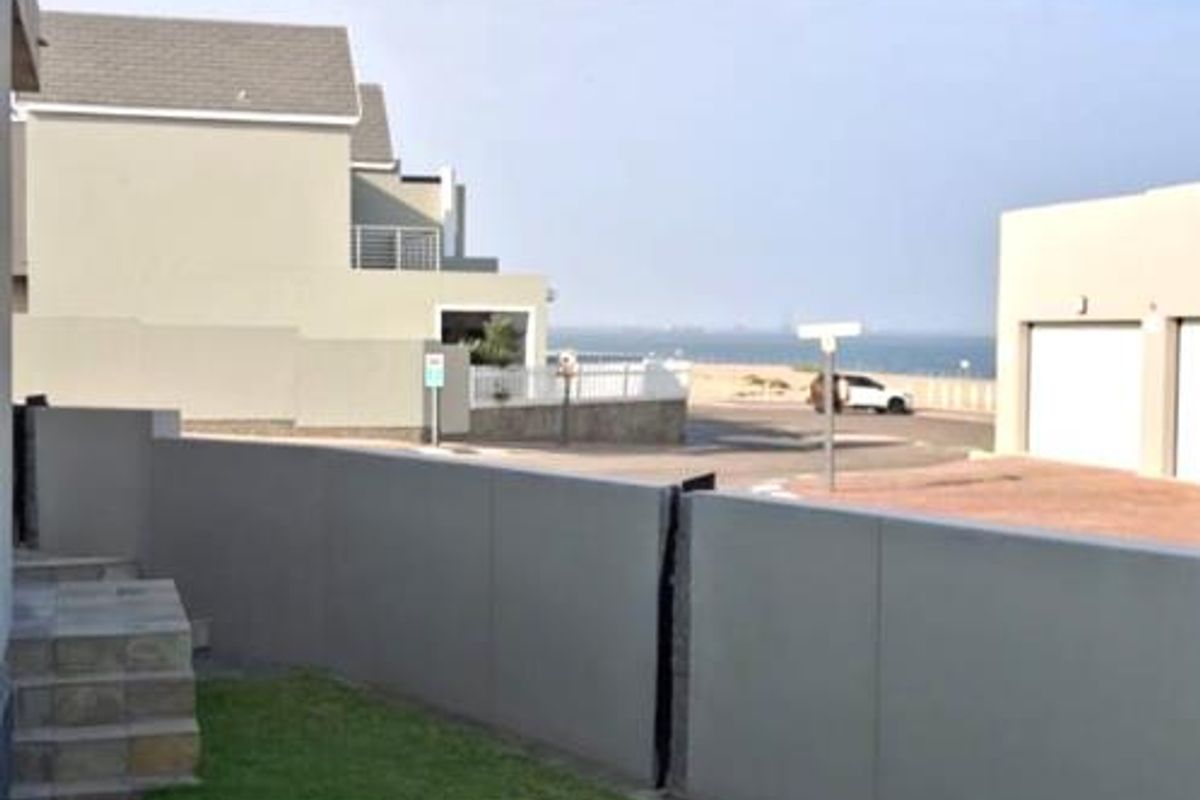 A rear exterior view of the townhouse featuring a private lawn, paved patio area, and stone steps leading to the property.