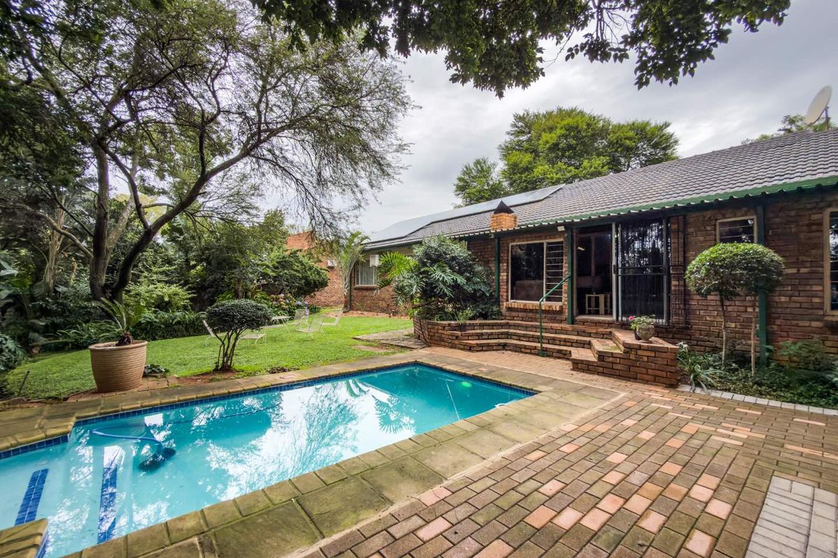 Rear garden featuring a swimming pool, brick-paved patio area, and established landscaping with mature trees.