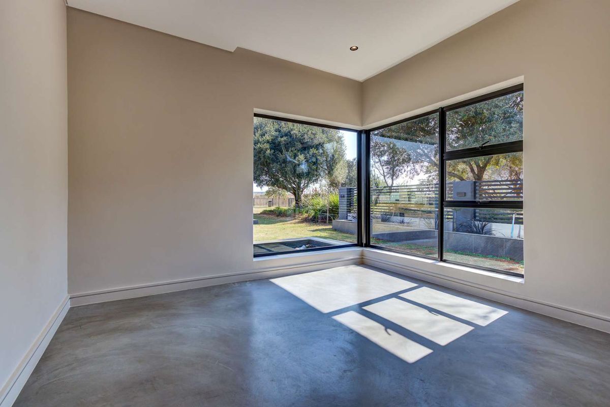 A bright, modern bedroom featuring polished concrete floors and a large corner window providing ample natural light and garden views.
