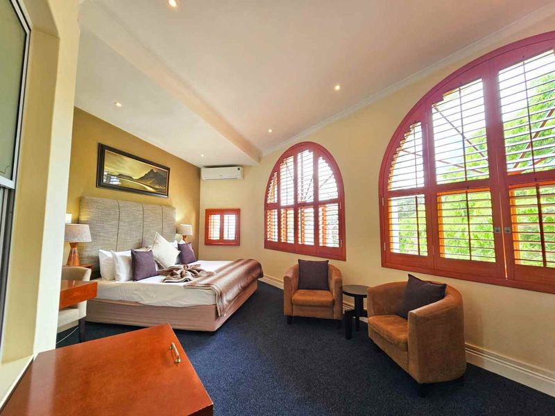 Spacious bedroom featuring arched windows with timber shutters, recessed lighting, and a split-system air conditioner.