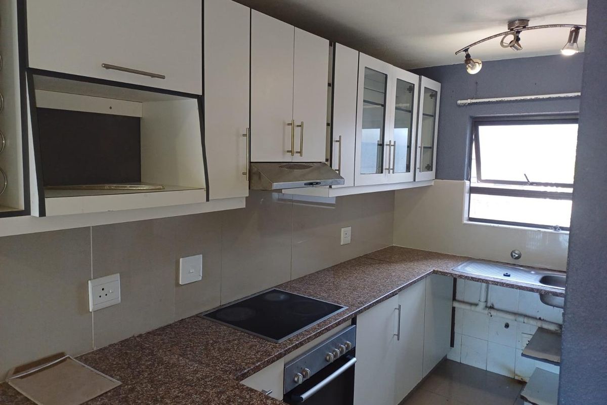 Functional kitchen featuring white cabinetry, granite countertops, built-in oven with hob, extractor fan, and a stainless steel sink with tiled splashback.