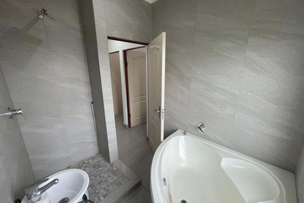 Modern bathroom featuring large format grey wall tiles, a corner bathtub, and a separate shower area with mosaic floor detailing.