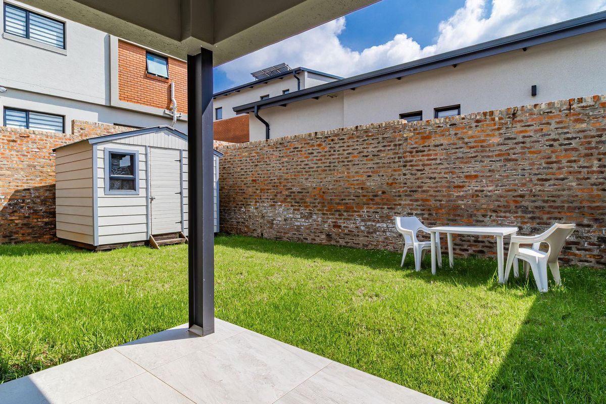 A private rear garden featuring a tiled patio area, a well-maintained lawn, and a brick boundary wall with an included storage shed.