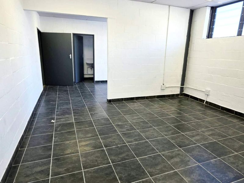 A clean, empty industrial office space featuring durable tiled flooring, exposed block walls, and natural light from high-level louvre windows.