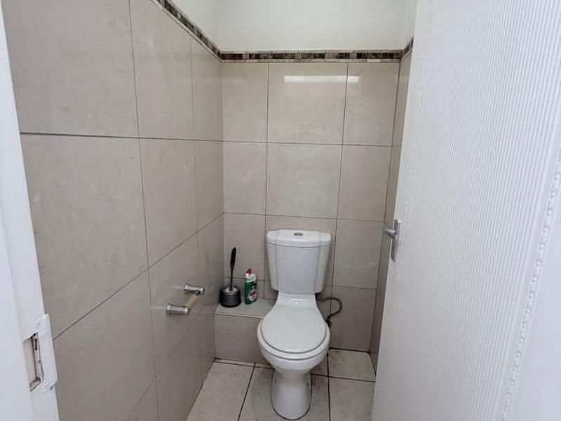 A clean and functional guest bathroom featuring neutral ceramic wall and floor tiles with a decorative border.