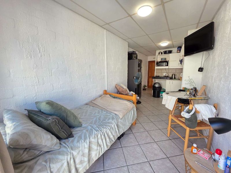Compact open-plan studio apartment featuring a kitchenette with built-in cabinetry, tiled flooring, and textured walls.