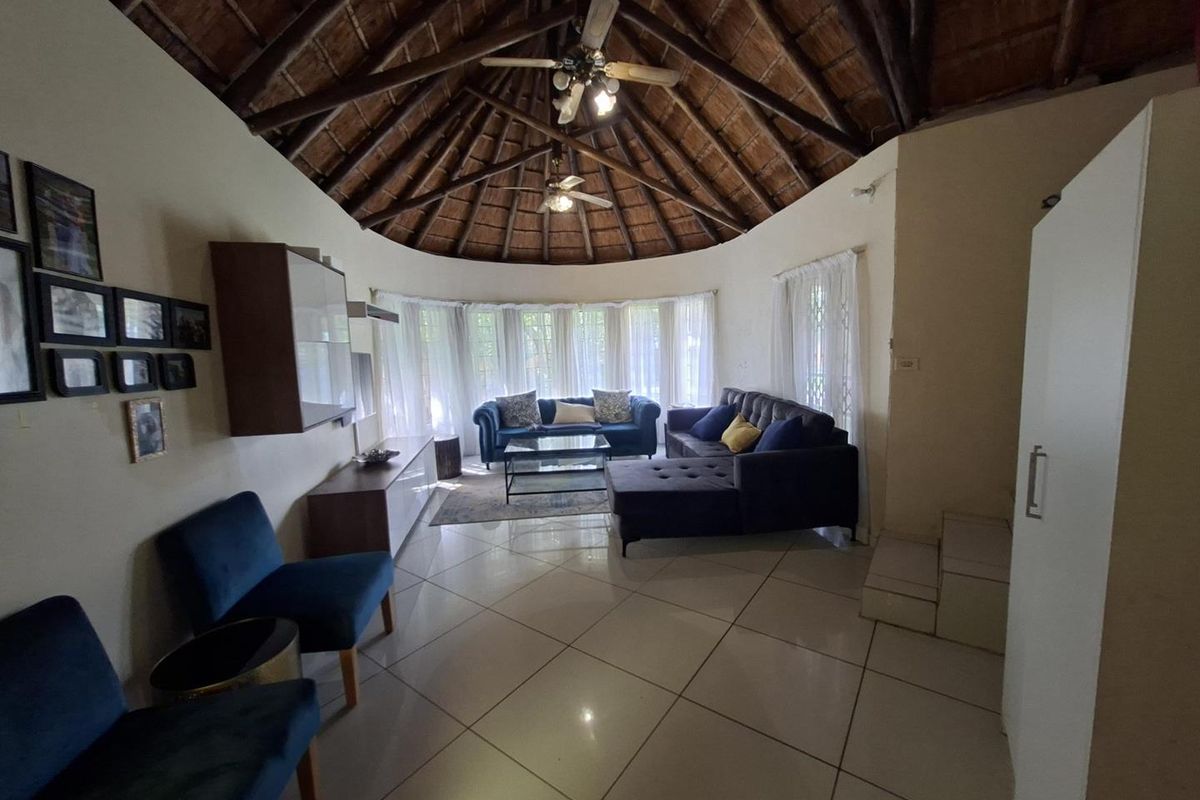 Spacious living room featuring a high vaulted thatched ceiling with exposed timber beams, tiled flooring, and large windows providing ample natural light.