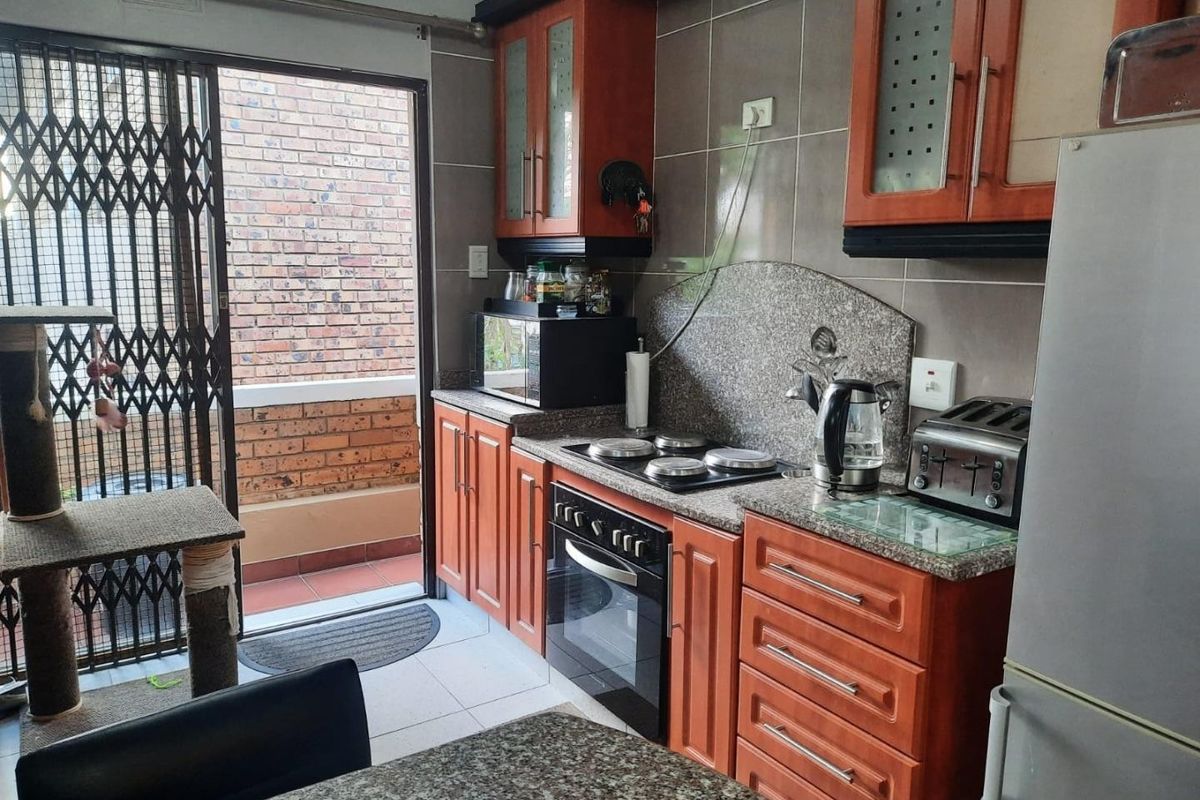 A functional kitchen featuring wood-finish cabinetry, granite countertops, built-in oven and hob, with direct access to an outdoor balcony area.