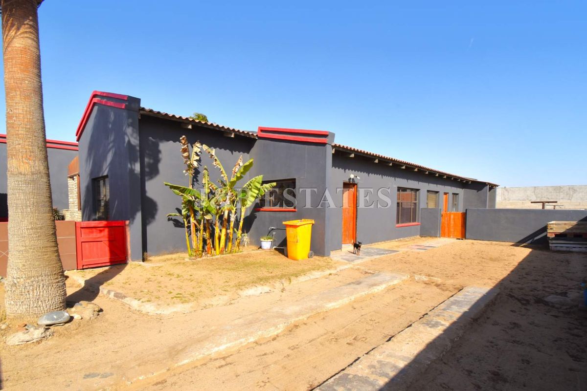 Rear view of the property featuring a dark-painted exterior facade, tiled roof, and an expansive unpaved outdoor area.