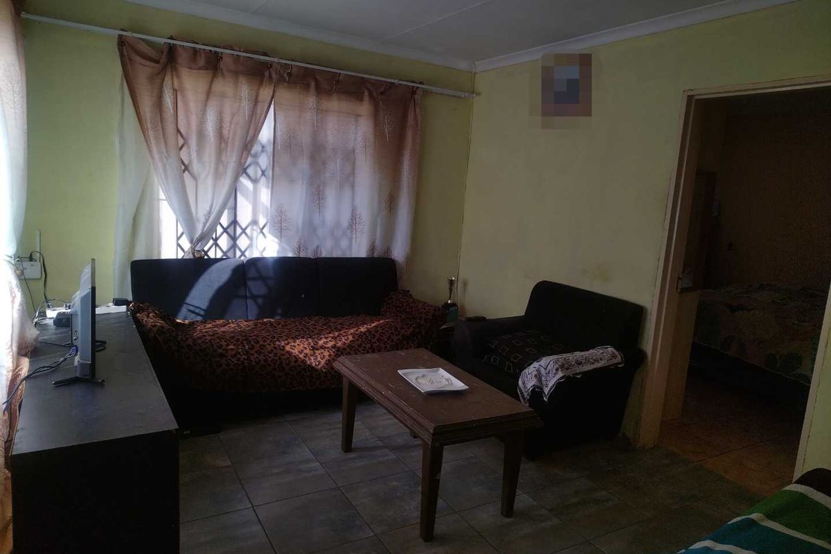 A living room featuring tiled flooring and a window with security bars, providing access to an adjacent bedroom.