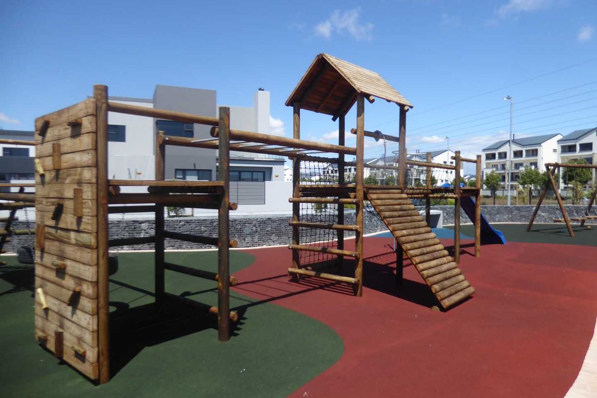 A well-maintained communal playground area featuring a wooden climbing structure, slide, and durable rubberized safety flooring within a residential estate.