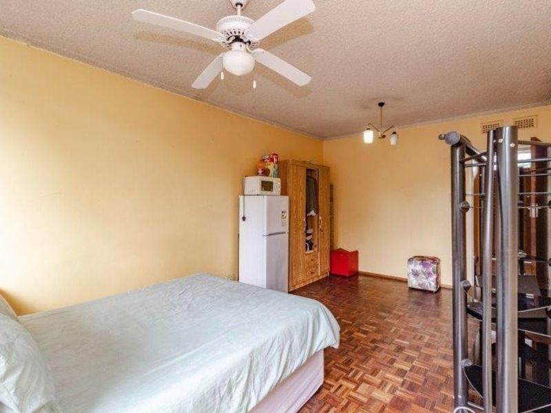A bedroom featuring parquet flooring, a ceiling fan, and textured ceilings. The space offers a functional layout with potential for cosmetic updates.