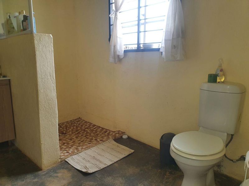 A functional bathroom featuring a toilet and a walk-in shower area with tiled flooring and security bars on the window.