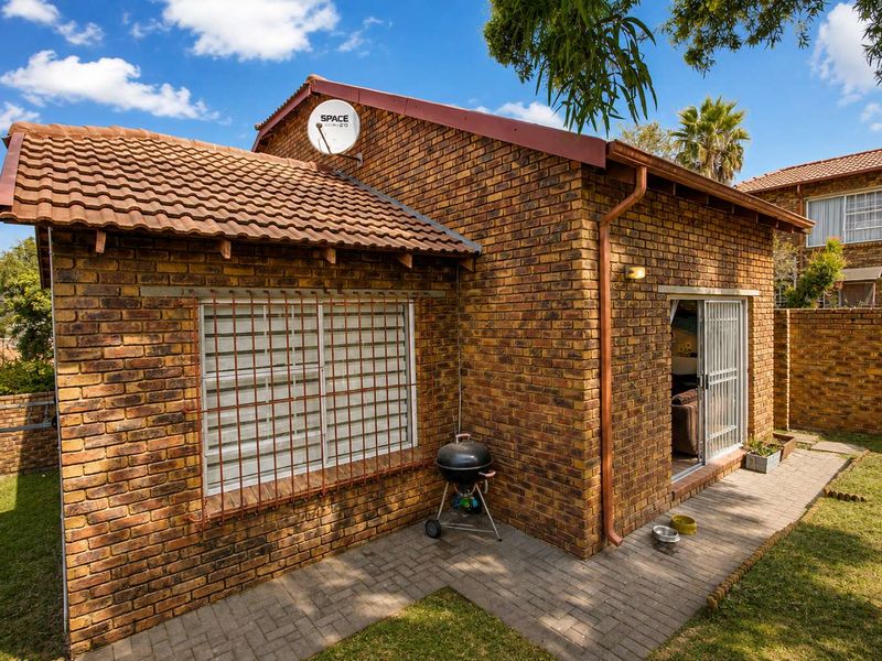 Rear view of a face brick townhouse featuring a paved patio area, sliding door access, and secure window bars.