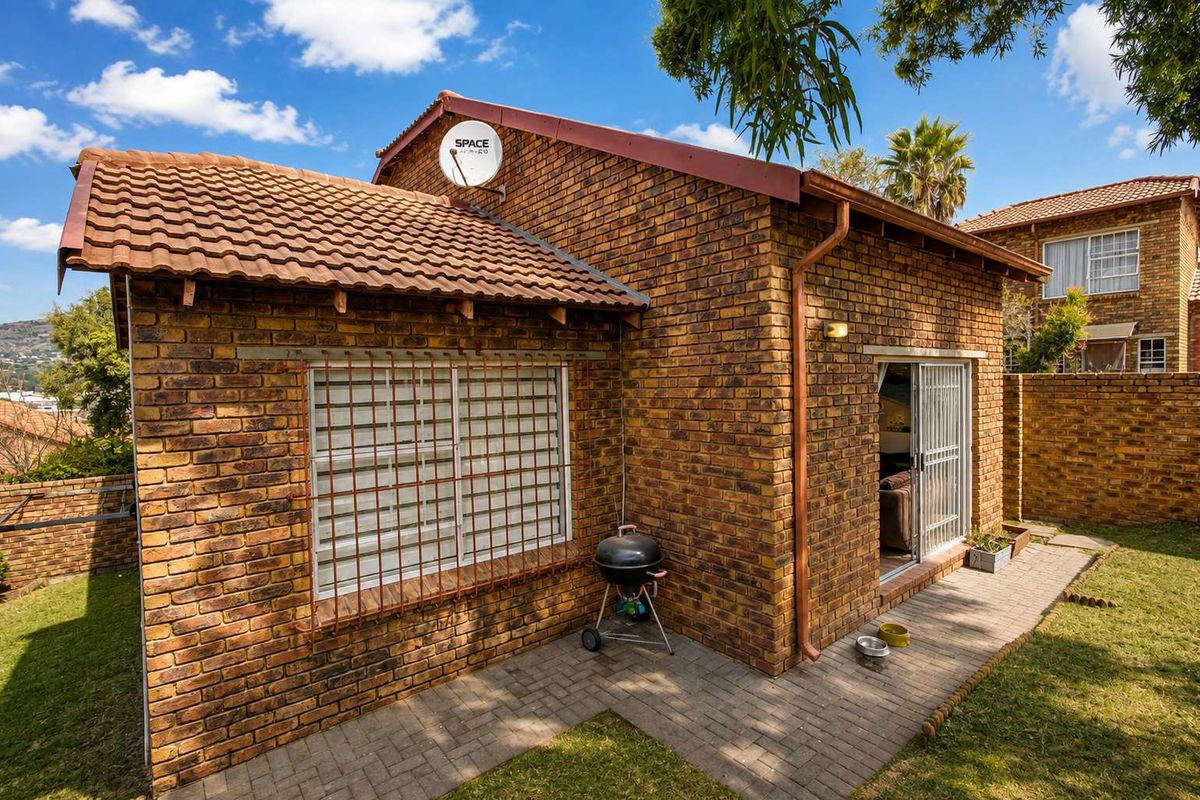 Rear view of a face brick townhouse featuring a paved patio area, sliding door access, and secure window bars.
