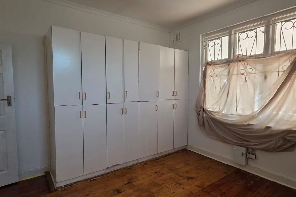 A vacant bedroom featuring built-in white cabinetry, original timber flooring, and windows fitted with security bars.