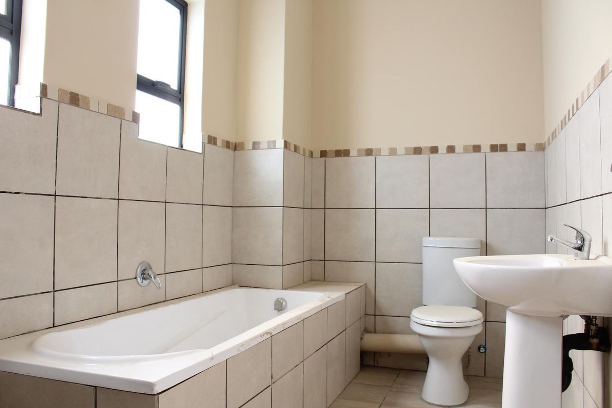 A functional bathroom featuring a built-in bathtub, pedestal basin, and toilet with neutral wall tiling and natural light from the window.