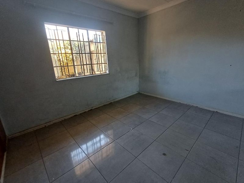 An empty bedroom featuring tiled flooring and a window fitted with security bars, requiring cosmetic updates to the wall finishes.