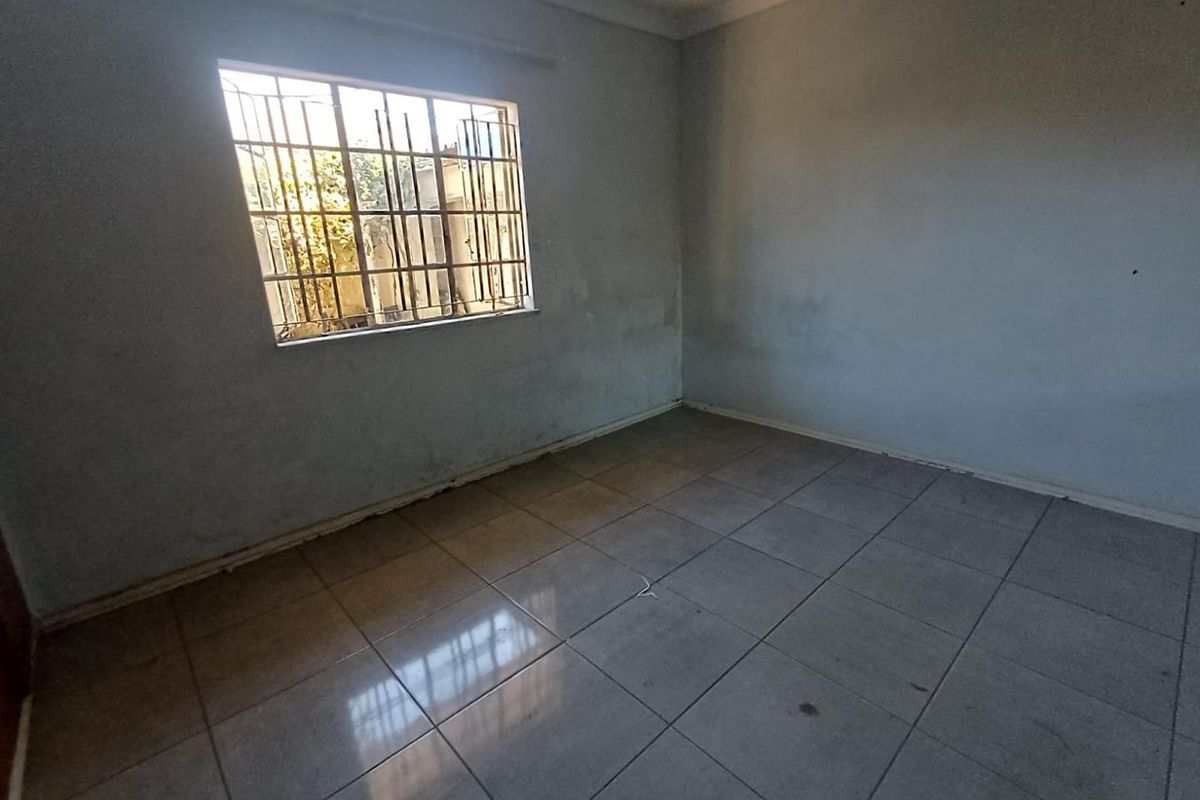 An empty bedroom featuring tiled flooring and a window fitted with security bars, requiring cosmetic updates to the wall finishes.