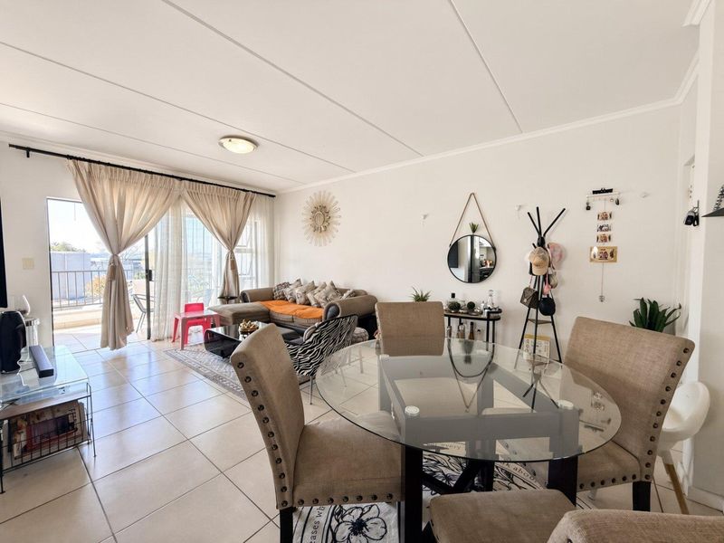 An open-plan living and dining area featuring tiled flooring, neutral walls, and a sliding glass door providing access to an outdoor balcony.