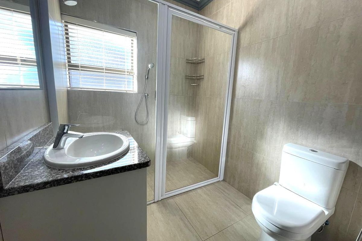 A clean, modern bathroom featuring a granite-topped vanity, a glass-enclosed shower, and a white toilet with neutral floor-to-ceiling wall tiles.