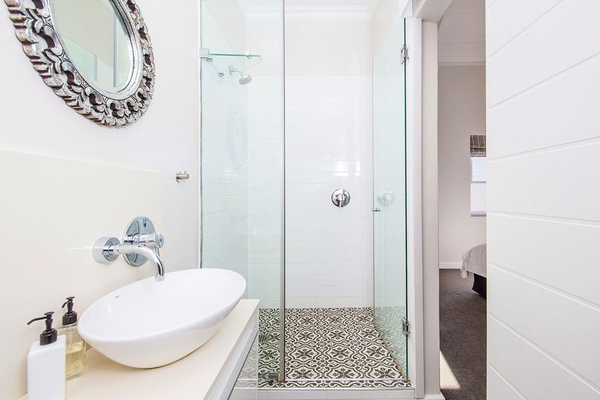 A modern bathroom featuring a glass-enclosed shower with patterned floor tiles, a wall-mounted basin, and chrome fixtures.