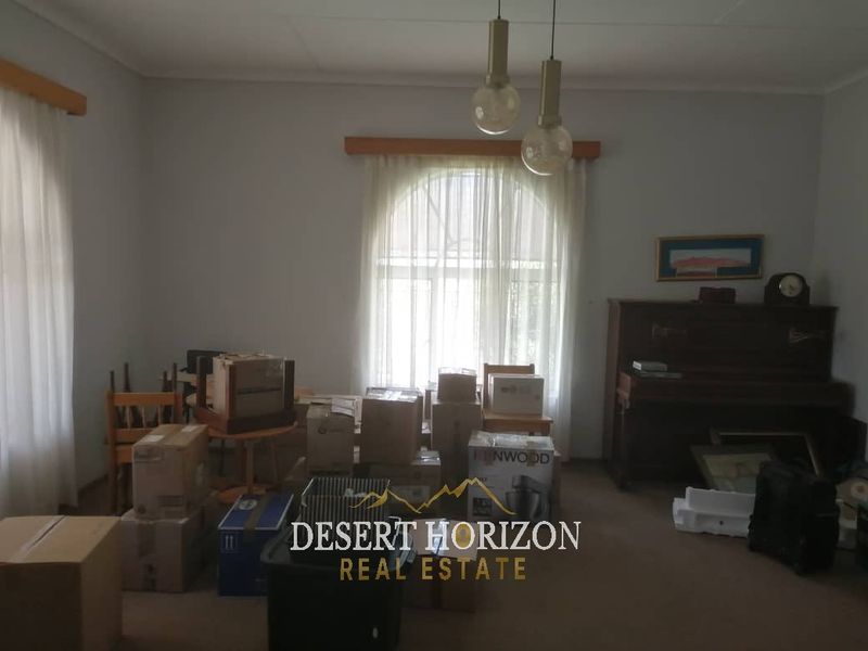 A living room space featuring neutral walls, carpeted flooring, and pendant lighting, currently used for storage.