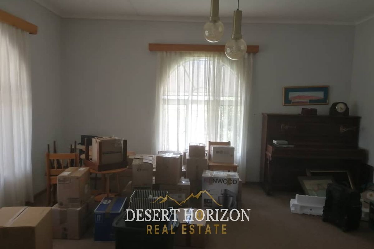 A living room space featuring neutral walls, carpeted flooring, and pendant lighting, currently used for storage.