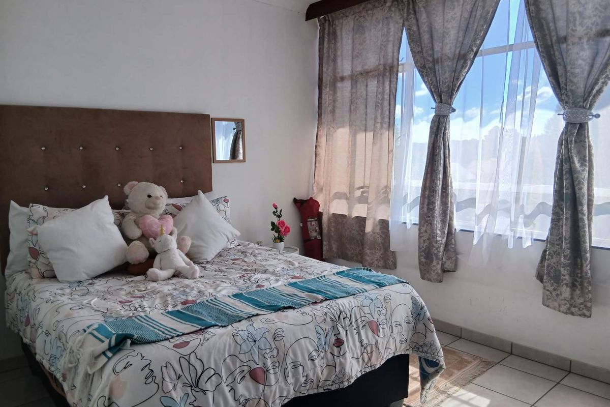 A bedroom featuring tiled flooring and a large window with curtain treatments, providing natural light to the space.