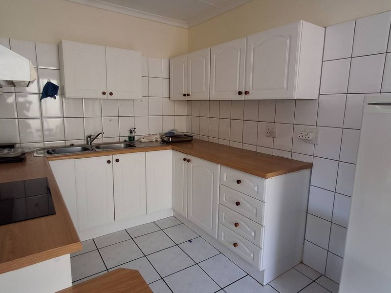 A functional kitchen featuring white cabinetry, laminate countertops, a double basin sink, and a tiled backsplash with a built-in electric hob and extractor fan.